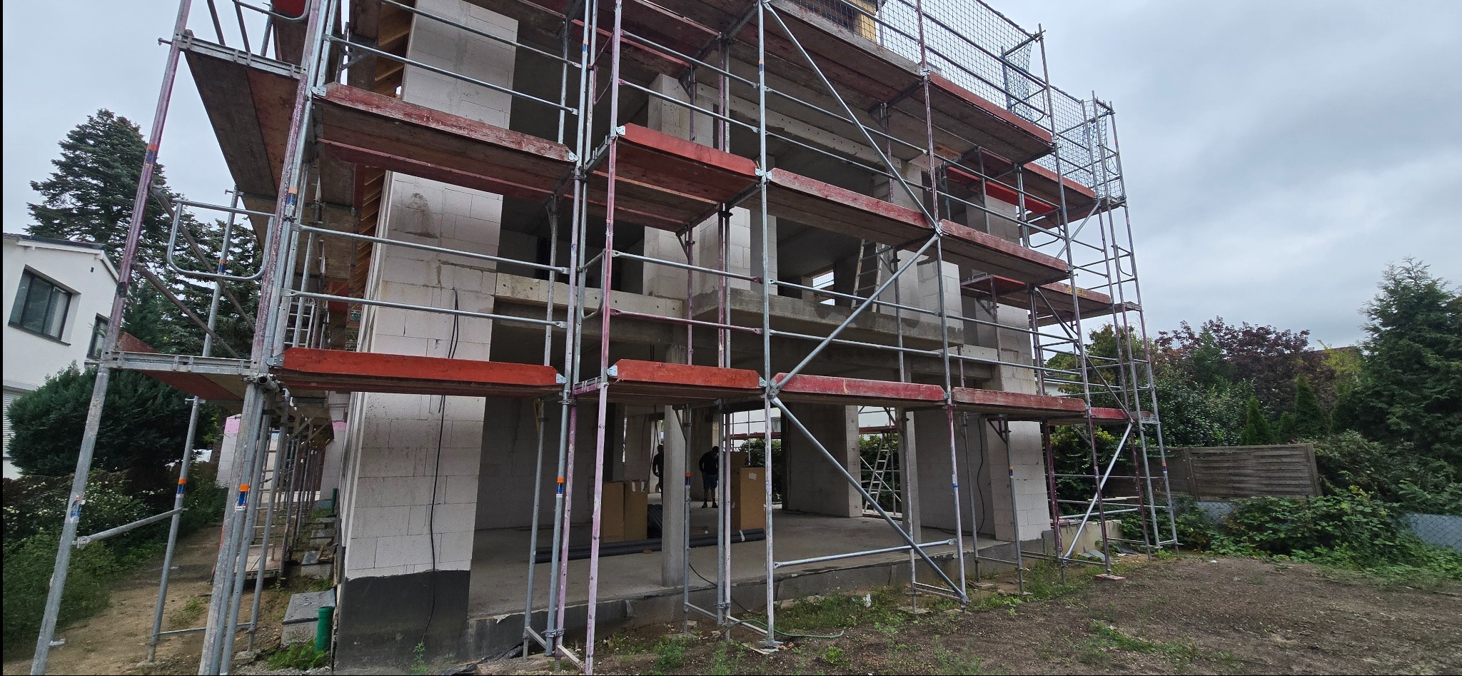 Surowy stan domu w trakcie budowy, z widocznymi rusztowaniami i pustakami. Stan surowy otwarty z widocznymi otworami okiennymi i drzwiowymi.