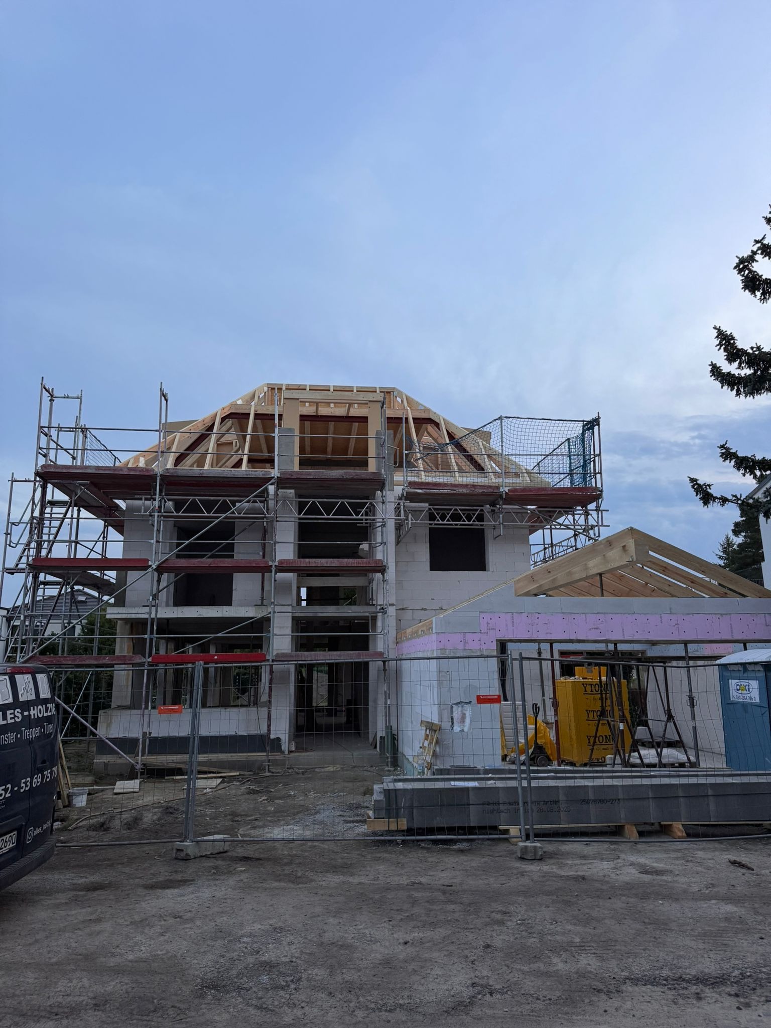 Budowa domu z białych bloczków, z widocznymi rusztowaniami i drewnianą konstrukcją dachu w trakcie montażu. Na pierwszym planie bloczki YTONG.