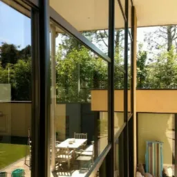 Nowoczesne okna aluminiowe z czarnymi ramami, widok z zewnątrz na taras z meblami ogrodowymi i zielony trawnik, po umyciu, z widocznymi smugami wody.