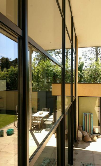 Nowoczesne okna aluminiowe z czarnymi ramami, widok z zewnątrz na taras z meblami ogrodowymi i zielony trawnik, po umyciu, z widocznymi smugami wody.