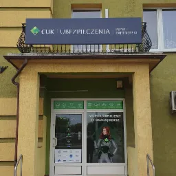 Fasada budynku CUK Ubezpieczenia z szyldem i wejściem, gdzie na drzwiach widnieje reklama z hasłem 'My porównujemy, Ty oszczędzasz'.