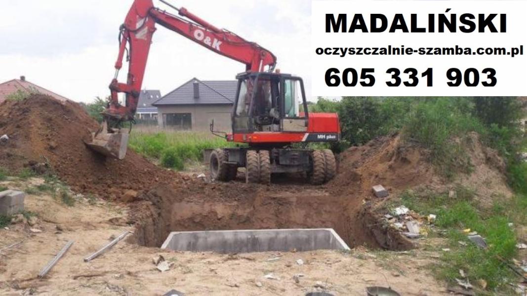 Czerwona koparka O&K MH plus podczas wykopu pod betonowy zbiornik, widoczny numer telefonu i adres strony internetowej firmy.
