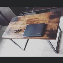 Biurko loftowe z blatem z postarzanego drewna i metalową podstawą, na blacie leżą okulary w czarnych oprawkach i zamknięty laptop Lenovo.