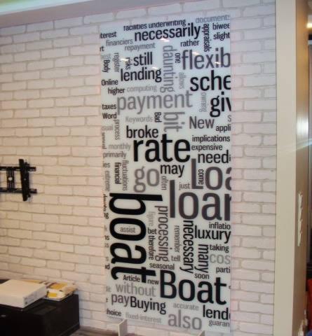 Szklana ścianka działowa z nadrukowanym motywem chmury słów o tematyce finansowej, umieszczona w biurze z białą ceglaną ścianą.