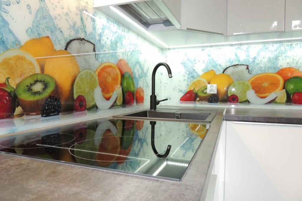 Szklany panel kuchenny z motywem owoców i błękitnych plam, zamontowany nad zlewem i płytą indukcyjną w nowoczesnej kuchni z białymi szafkami.