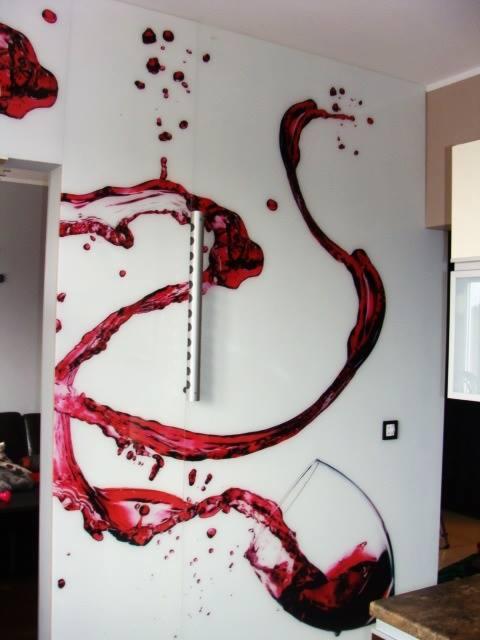 Szklana ściana z nadrukiem przedstawiającym rozlane czerwone wino z kieliszka, nowoczesny design w jasnym wnętrzu.