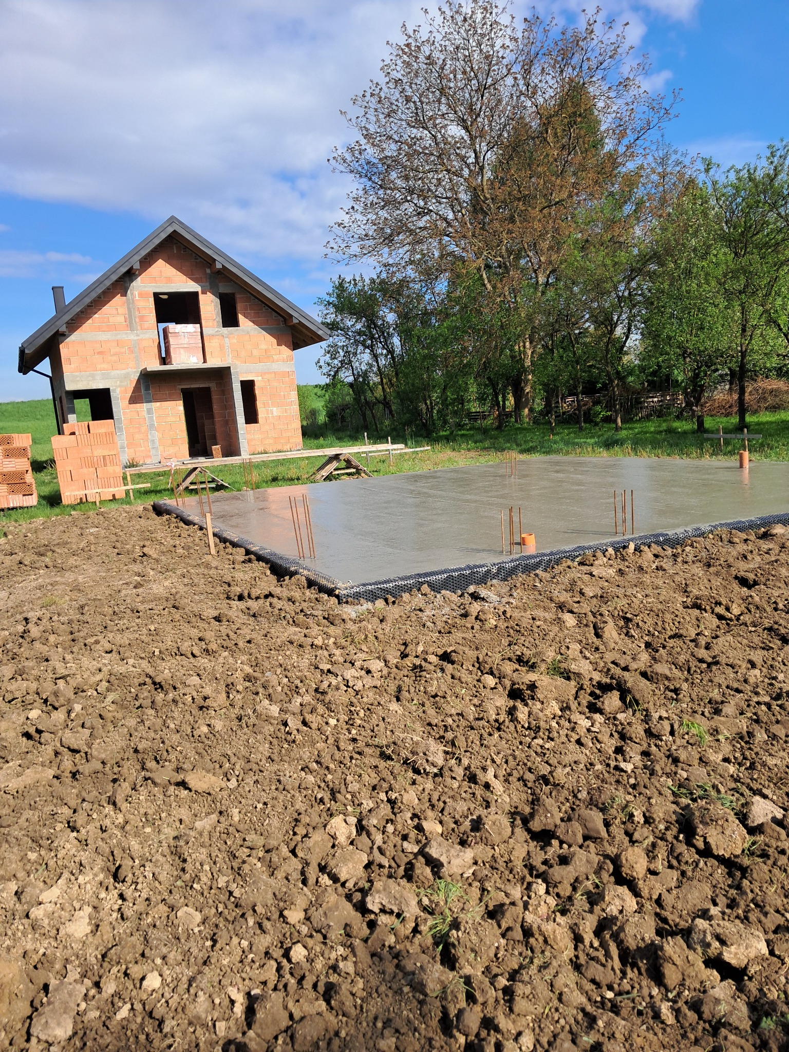 Wylana płyta fundamentowa pod dom murowany w otoczeniu zieleni, ściany domu w stanie surowym otwartym, widok na plac budowy w słoneczny dzień.