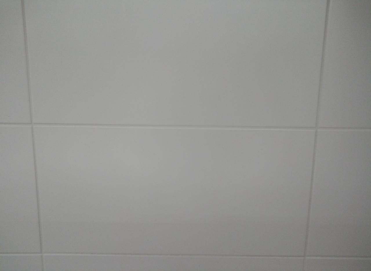 Jasnoszare, matowe płytki ceramiczne ułożone na ścianie, widoczne fugi o minimalnej szerokości.