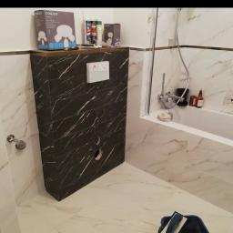 R-B TEAM - Łazienka z białymi marmurowymi płytkami i czarną obudową podtynkową WC z marmurowym wzorem, widoczne puszki z farbami i narzędzia glazurnicze.