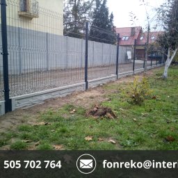 FONREKO - Szary panelowy płot z podmurówką na posesji, widok z boku. Elementy złączone śrubami. W tle dom z czerwonym dachem i drzewa.