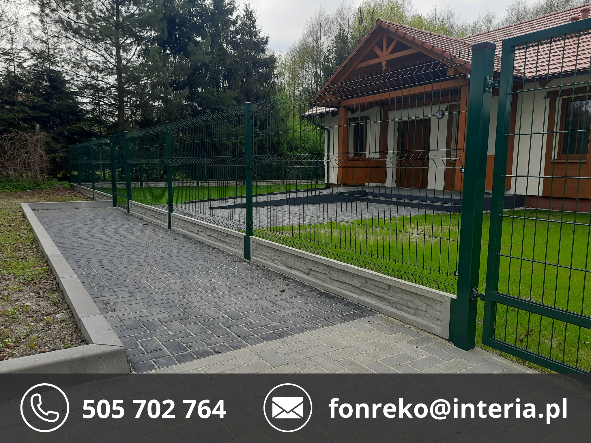 Zielone ogrodzenie panelowe z bramą, z podmurówką, na tle domu z brązowym dachem i zieleni. Kostka brukowa prowadzi wzdłuż ogrodzenia.