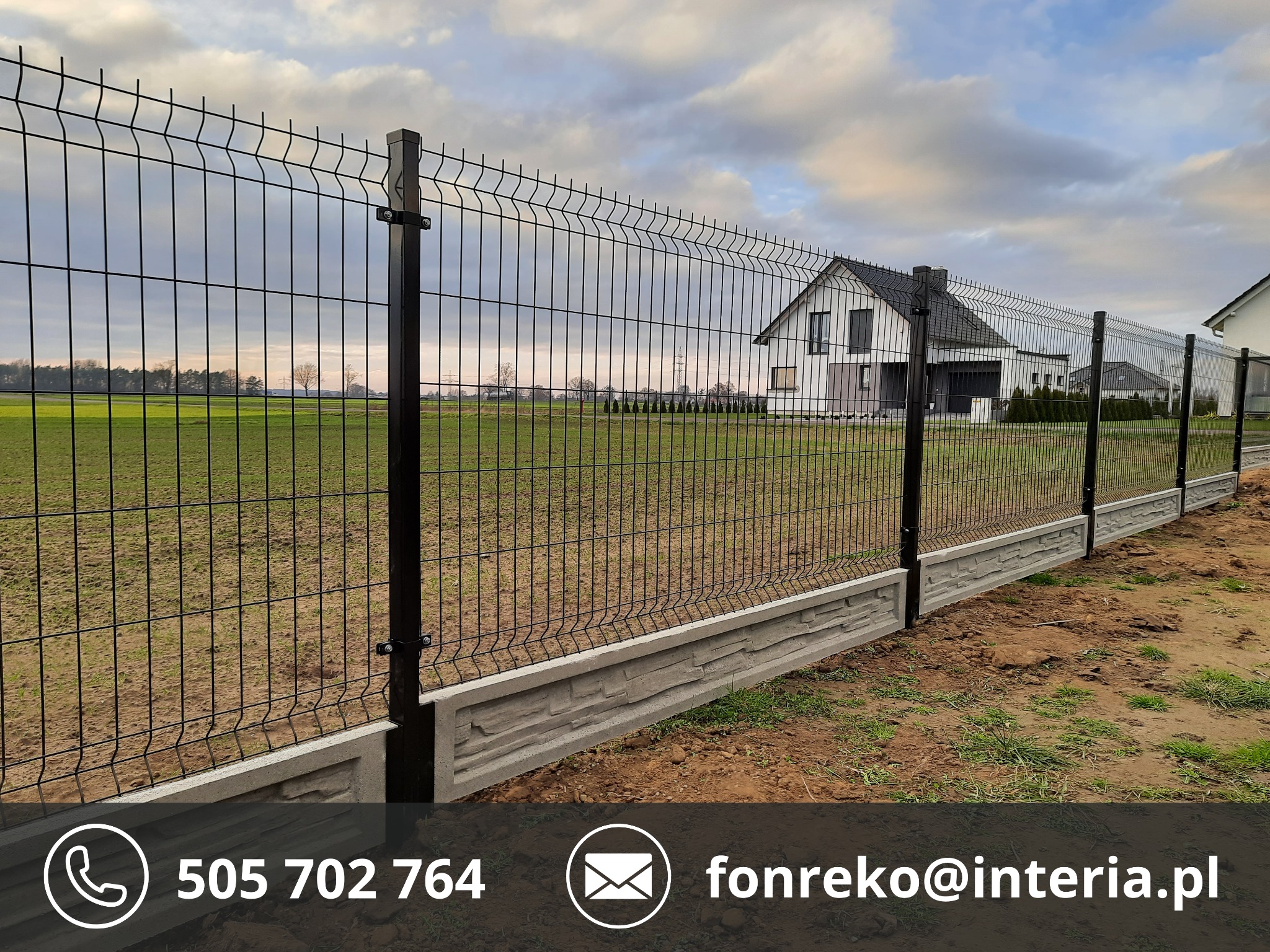 Czarne ogrodzenie panelowe z podmurówką o fakturze kamienia na tle zielonego pola i domu. Słupki ogrodzeniowe z kwadratowymi zakończeniami.