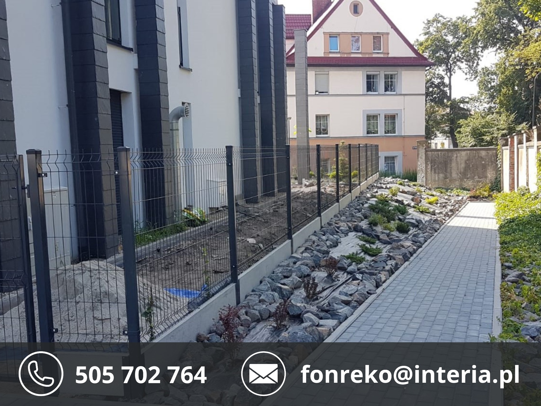 Nowoczesne ogrodzenie panelowe w kolorze grafitowym, oddzielające posesję od chodnika. W tle budynek mieszkalny i zagospodarowana przestrzeń z kamieniami i roślinami.