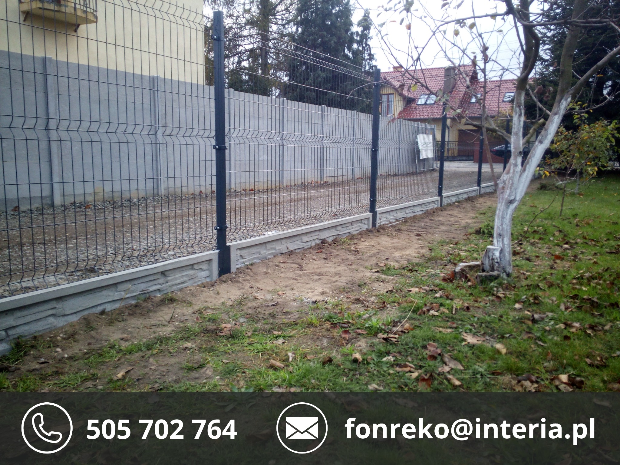 Szary panelowy płot z betonową podmurówką, widok z boku na tle domu z czerwoną dachówką i drzewa z bielonym pniem. Jesienne liście na trawie.