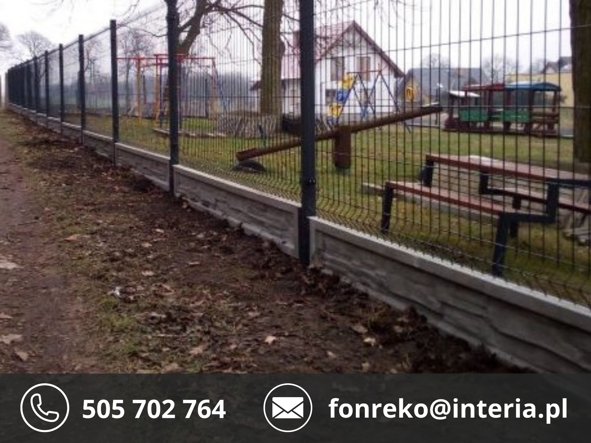 Długi, czarny panelowy płot z betonową podmurówką, zabezpieczający plac zabaw z huśtawkami i drewnianą lokomotywą w tle. Widok z niskiej perspektywy.