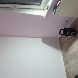 Pokój po świeżym malowaniu z różowym sufitem skosnym, widoczne narzędzia i lampa na podłodze z paneli.