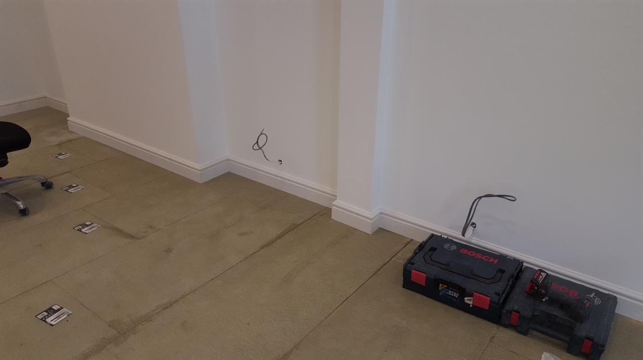Przygotowanie do położenia parkietu: widoczne płyty izolacyjne na podłodze, listwy przypodłogowe, puszka elektryczna wystająca ze ściany oraz skrzynki z narzędziami Bosch.