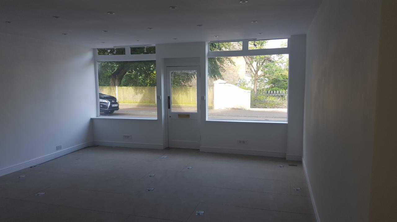 Wnętrze pomieszczenia po świeżym malowaniu na biało, widoczne okna z widokiem na ulicę i samochód, podłoga przygotowana do dalszych prac wykończeniowych.