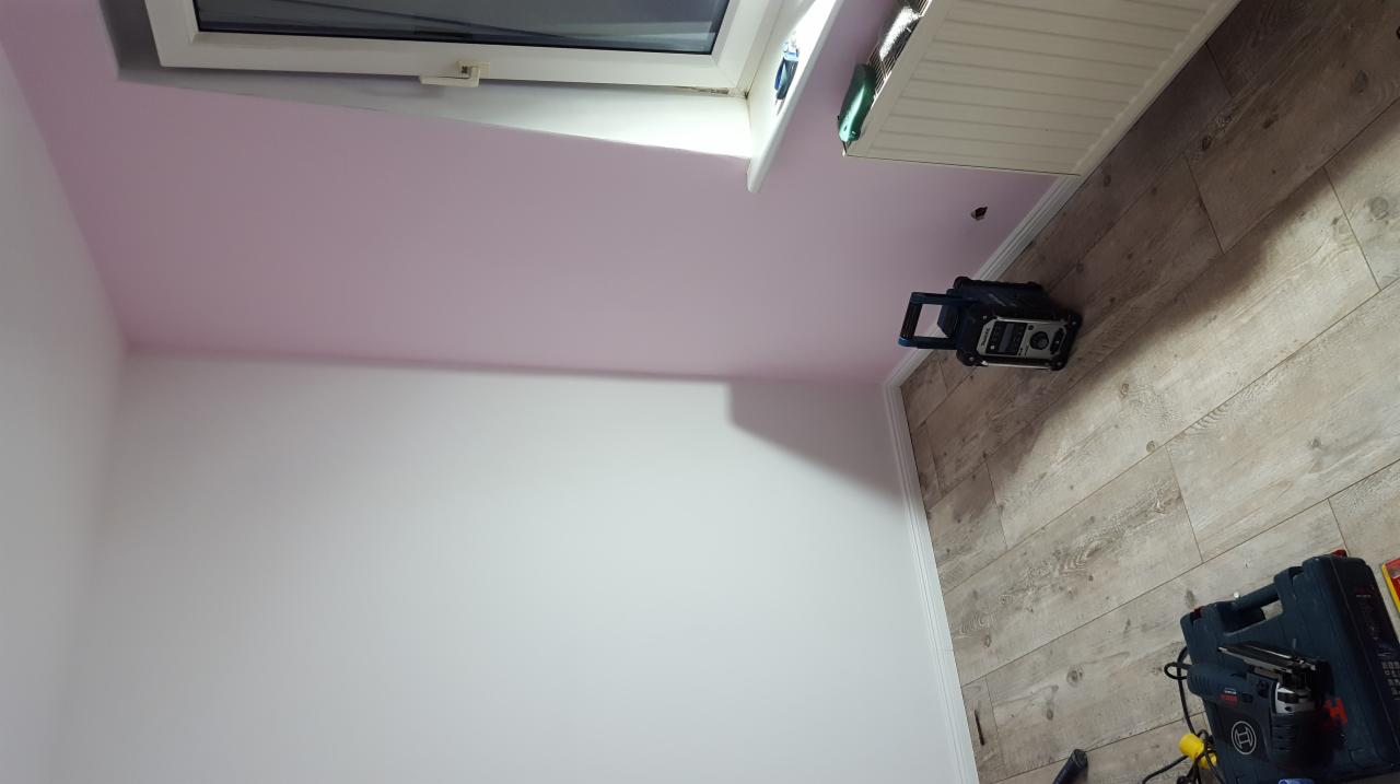Pokój po świeżym malowaniu z różowym sufitem skosnym, widoczne narzędzia i lampa na podłodze z paneli.