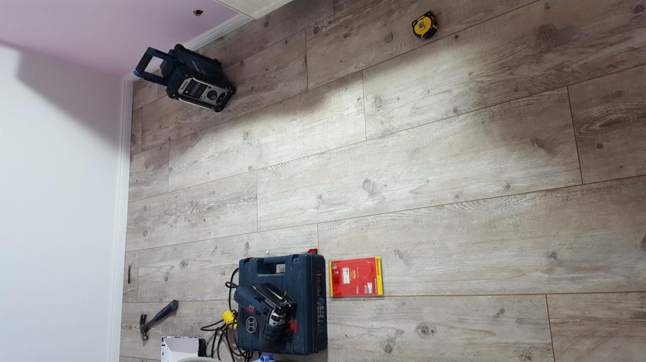 Przygotowanie do montażu paneli ściennych: narzędzia, skrzynka narzędziowa i poziomica laserowa na tle ściany wyłożonej panelami imitującymi drewno.