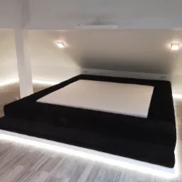 Podwyższone, czarne, tapicerowane łóżko z pikowanym obiciem i podświetleniem LED w minimalistycznej sypialni ze skosami.