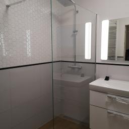 MT2 - Nowoczesna łazienka z kabiną prysznicową typu walk-in, heksagonalnymi płytkami na ścianie i szafką pod umywalką z folią ochronną na uchwytach szuflad.