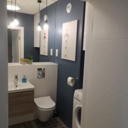 MT2 - Nowoczesna łazienka z ciemnoniebieską ścianą, wzorzystą podłogą, umywalką z drewnianą szafką, toaletą, pralką Electrolux i obrazami latarni morskich.