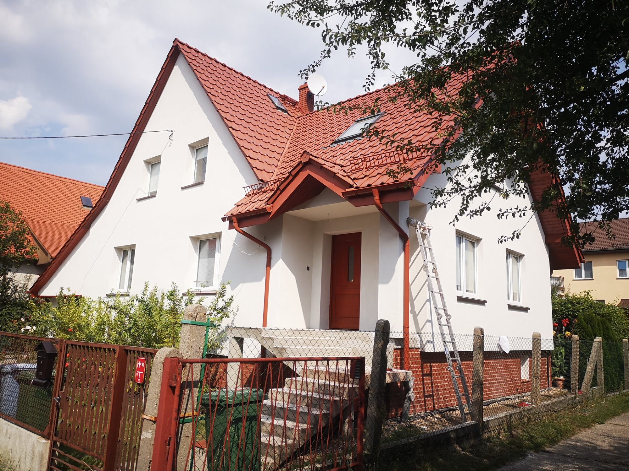 Biały dom jednorodzinny z czerwoną dachówką i stolarką okienną, po renowacji elewacji, z rozstawioną drabiną przy ścianie.