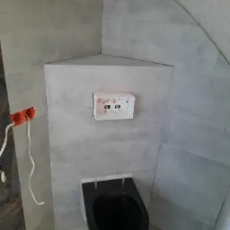 Montaż podtynkowego stelaża WC z czarną miską wiszącą na tle szarych płytek, widoczne przewody elektryczne i niedokończone prace wykończeniowe.