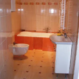 Wykończona łazienka w Bydgoszczy z beżowymi płytkami podłogowymi z brązowymi akcentami, białą wanną w obudowie, bidetem i umywalką z szafką oraz grzejnikiem drabinkowym.