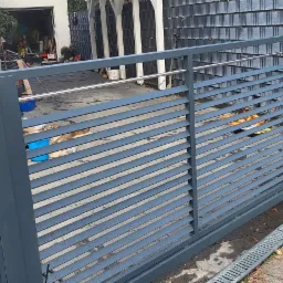 Szara, przesuwna brama wjazdowa z poziomymi panelami, widok z zewnątrz, z widocznym podjazdem i garażem w tle.