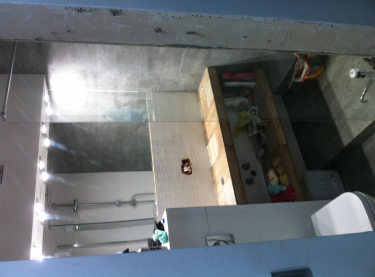 Wnętrze łazienki w trakcie prac wykończeniowych, widoczne białe płytki na ścianach, surowy betonowy sufit, instalacje sanitarne i elektryczne w trakcie montażu, oraz częściowo umeblowana przestrzeń...