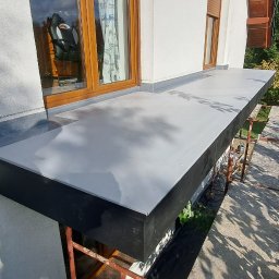 ArtHouse Artur Grzyb - Wykończony balkon z szarą, gładką powierzchnią, widok z góry, rusztowanie w tle, okno z drewnianą ramą i zasłoną z motywem samolotów