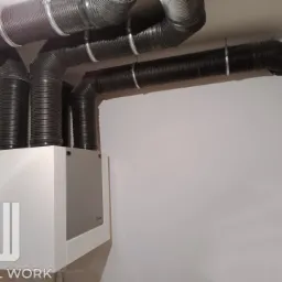 Zamontowany rekuperator Vasco z podłączonymi przewodami wentylacyjnymi, widoczne obejmy mocujące przewody do sufitu.