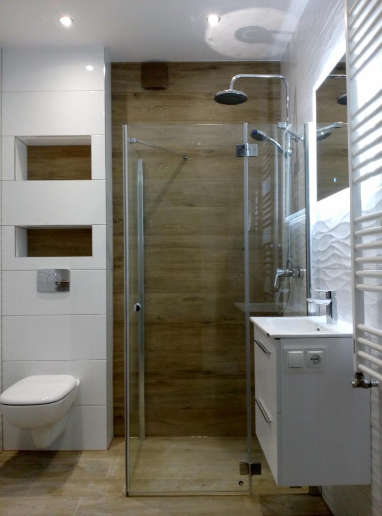 Nowoczesna łazienka z kabiną prysznicową typu walk-in, wykończona białymi i drewnopodobnymi płytkami, z podtynkową armaturą i minimalistyczną umywalką.