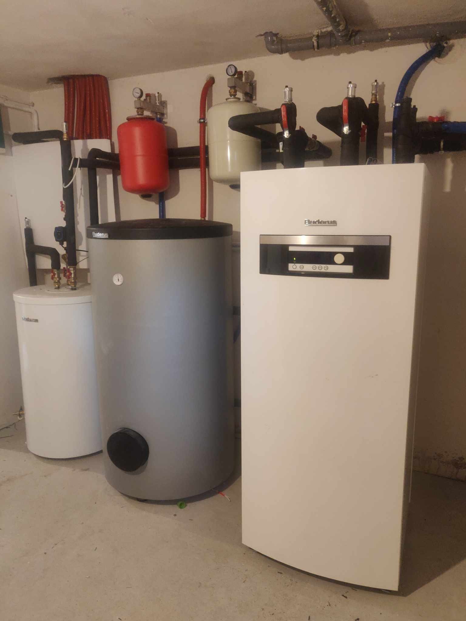 Kotłownia z trzema zbiornikami, w tym jeden z panelem sterowania marki Buderus, oraz instalacją rur miedzianych i czarnych.