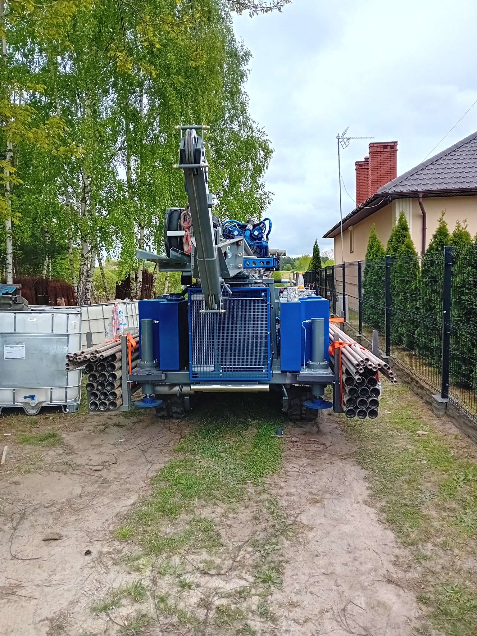 Wiertnica do studni głębinowych na posesji, widoczne rury wiertnicze i zbiorniki na wodę.