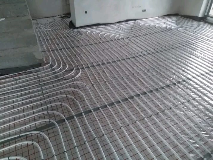 Białe rury ogrzewania podłogowego ułożone na siatce, widok z góry, surowy stan wykończenia wnętrza, przygotowanie do wylewki.