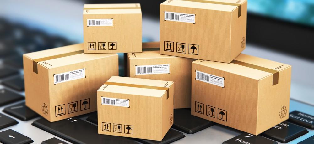 Stos kartonowych pudeł z etykietami i symbolami ostrożnego obchodzenia się, ułożonych na klawiaturze komputera.