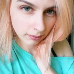 Portret kobiety z jasnoróżowymi włosami, ubranej w turkusową bluzkę z błyszczącymi aplikacjami, z delikatnym makijażem oczu i ust.