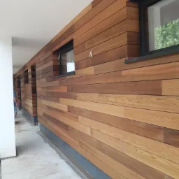 Elewacja budynku wykończona poziomymi deskami z jasnego drewna, z czarnymi ramami okiennymi, widok z zewnątrz, z boku budynku.