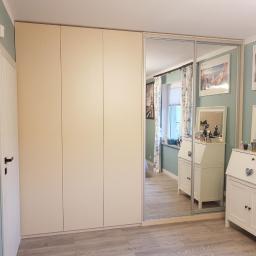 Damian Kycia - Beżowa szafa przesuwna z lustrem wkomponowana w ścianę, odbijająca fragment pokoju z dwoma białymi sekretarzykami i dekoracjami.