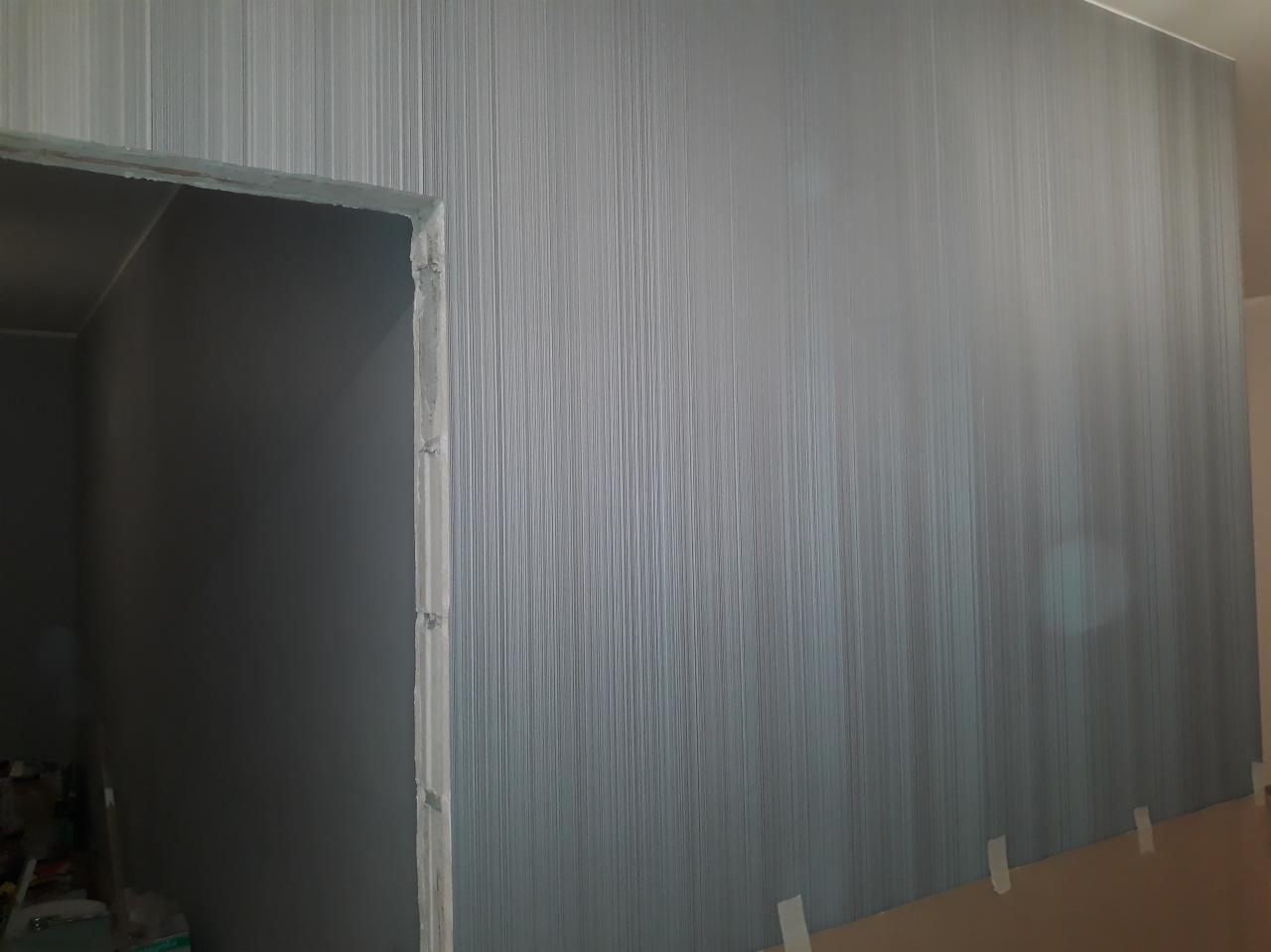 Świeżo wykończona ściana z tapetą w pionowe prążki w odcieniach szarości, widok na surowy otwór drzwiowy w Ząbkach.