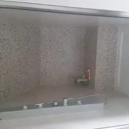 Niedokończona kabina prysznicowa z mozaiką na ścianach, widoczne elementy armatury i odpływ w brodziku, na półce leżą narzędzia i kosmetyki.