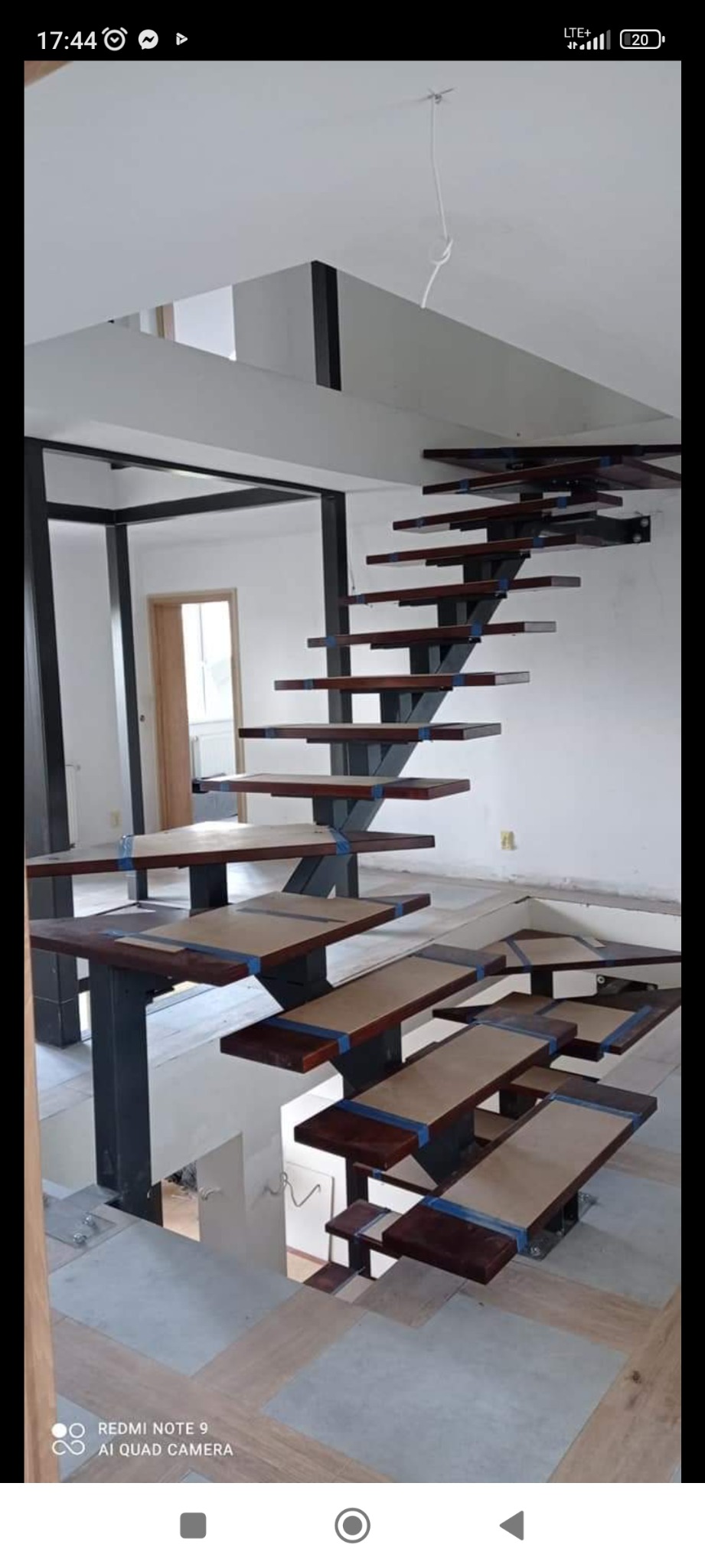 Ażurowe schody z drewnianymi stopniami i metalową konstrukcją nośną w trakcie montażu, zabezpieczone kartonem i niebieską taśmą.