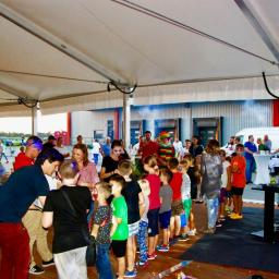 Wojciech Matkowski - Dzieci ustawione w kolejce pod namiotem podczas imprezy plenerowej, w tle widoczny klaun i osoba z makijażem, prawdopodobnie animatorzy.