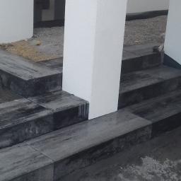 BolczasBruk - Schody i obrzeże z ciemnej, marmurkowatej kostki, częściowo ułożone, z widocznymi elementami konstrukcyjnymi i śladami zaprawy.