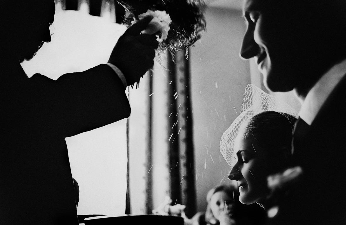 Czarno-białe zdjęcie profilu panny młodej w welonie, na którą sypią się płatki kwiatów podczas ceremonii ślubnej.