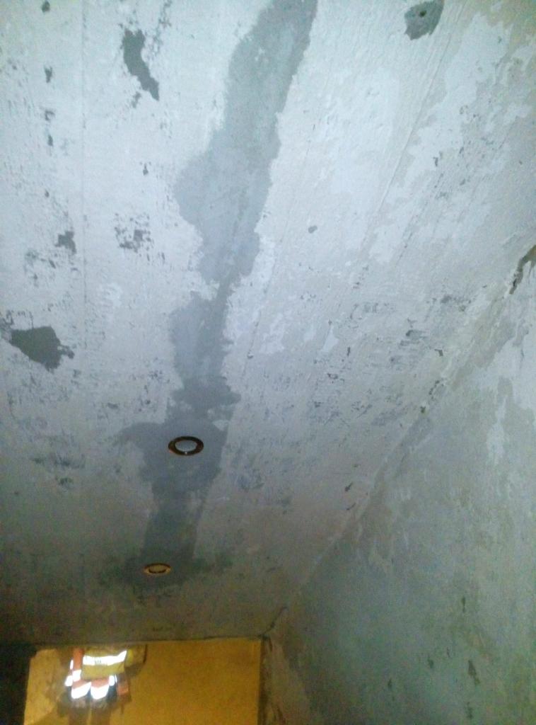 Surowy sufit i ściany w trakcie remontu z widocznymi śladami wilgoci i dwoma otworami na oświetlenie punktowe.