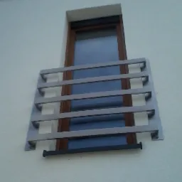 Zewnętrzna, metalowa barierka okienna z poziomych profili zamontowana na elewacji budynku, widok z dołu.